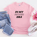 a pink shirt that says in my partner era next to a pair of jeans and